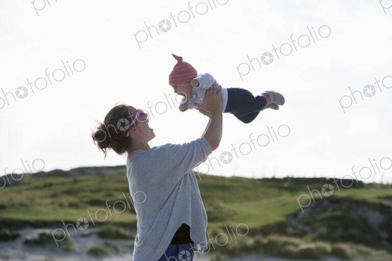 A mother raising her baby in the air. At the seaside.