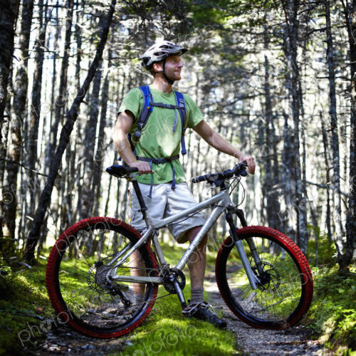 A mountain biker in a helmet with a rucksack standing by his bicycle in woodland.