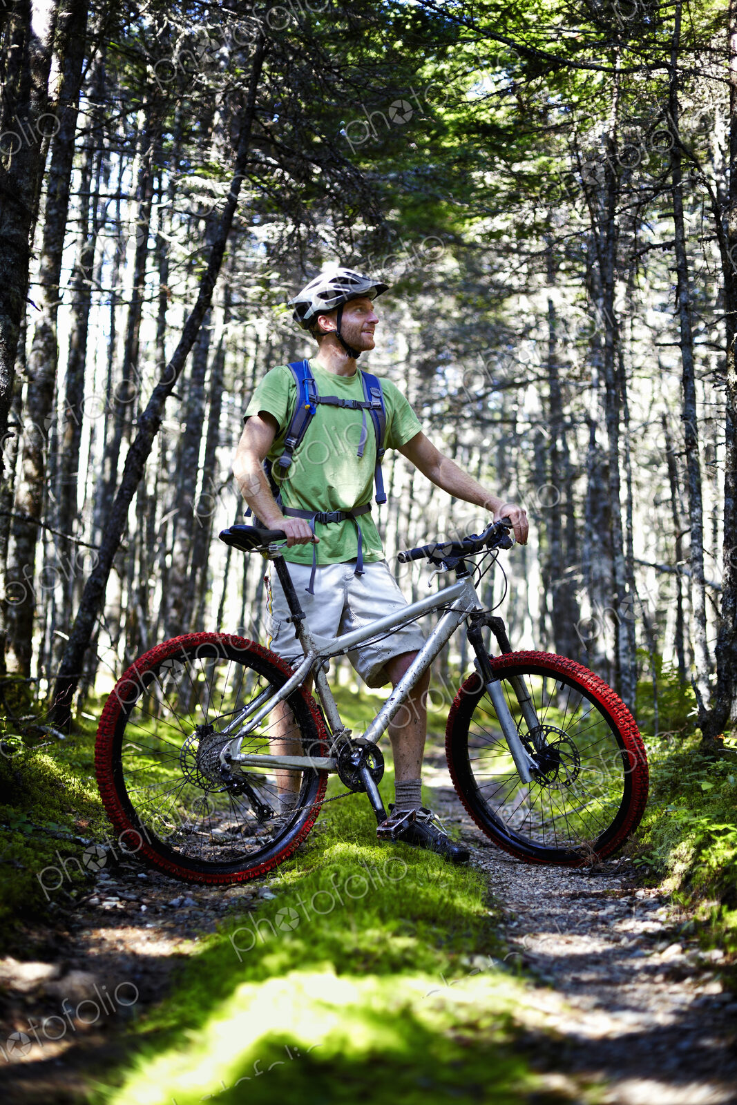 A mountain biker in a helmet with a rucksack standing by his bicycle in woodland.