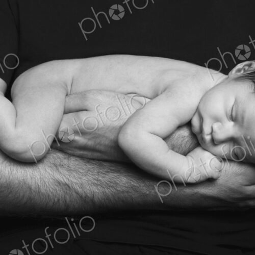 A naked newborn baby sleeping in his father's arms. A naked newborn baby sleeping in his father's arms.
