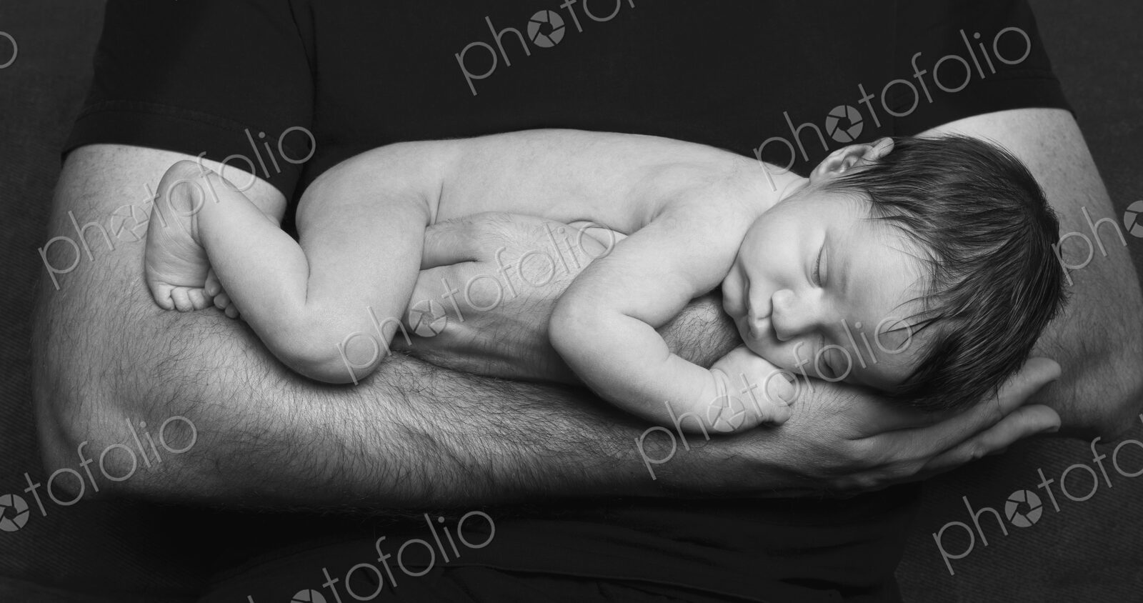 A naked newborn baby sleeping in his father’s arms.