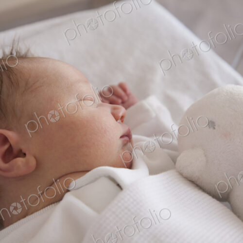 A new born baby lying on her back, sleeping. A toy in his cot.