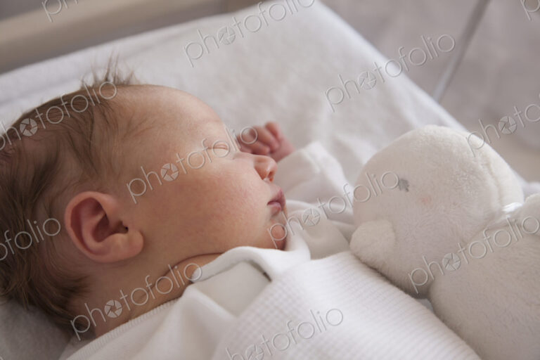 A new born baby lying on her back, sleeping. A toy in his cot.