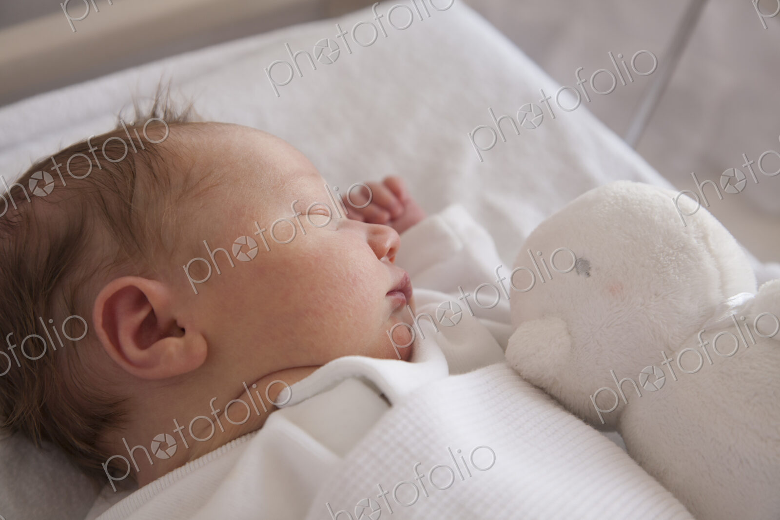 A new born baby lying on her back, sleeping. A toy in his cot.