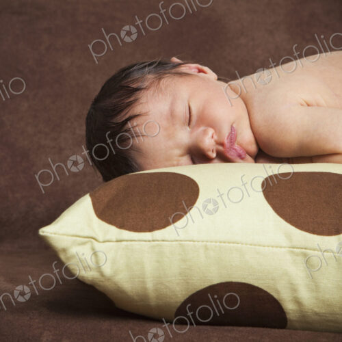 A newborn baby with his head turned to one side, lying sleeping on a polka dotted pillow. A newborn baby with his head turned to one side, lying sleeping on a polka dotted pillow.