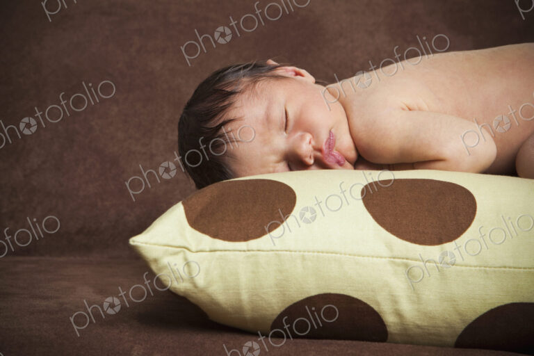 A newborn baby with his head turned to one side, lying sleeping on a polka dotted pillow.