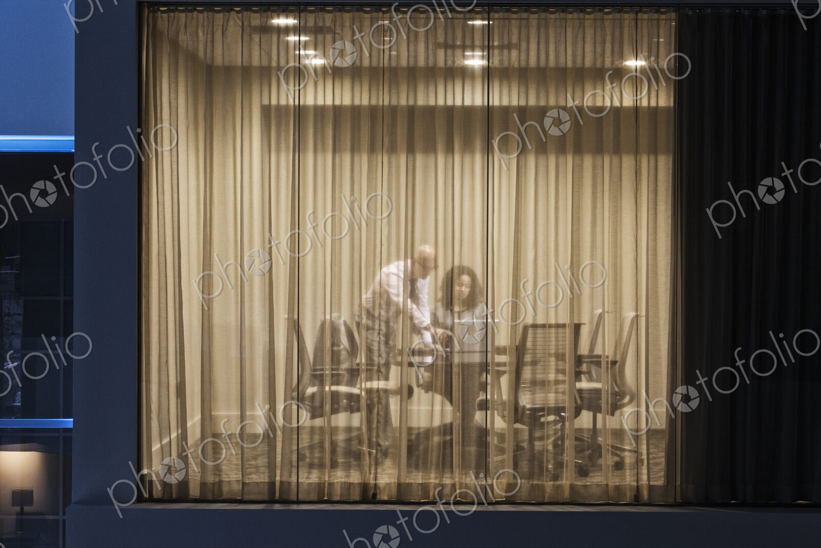 A night view looking into a conference room with two businesspeople working at…