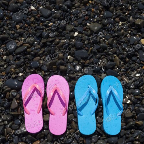 A pair of pink flip flops and a pair of blue flip flops lie side-by-side on a rocky… A pair of pink flip flops and a pair of blue flip flops lie side-by-side on a rocky…