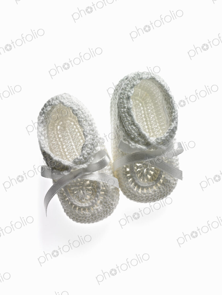 A pair of white baby booties, shoes for infants.