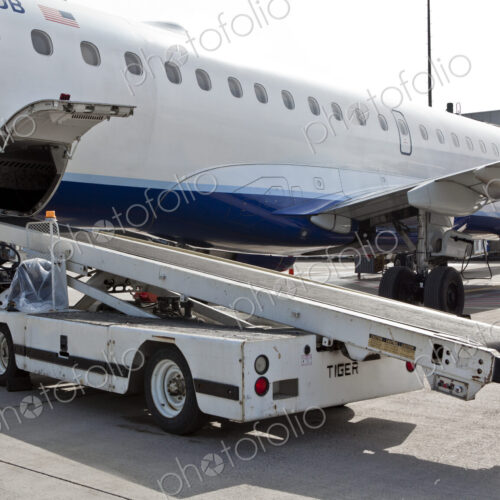 A passenger aircraft on a jetway with a baggage truck vehicle.