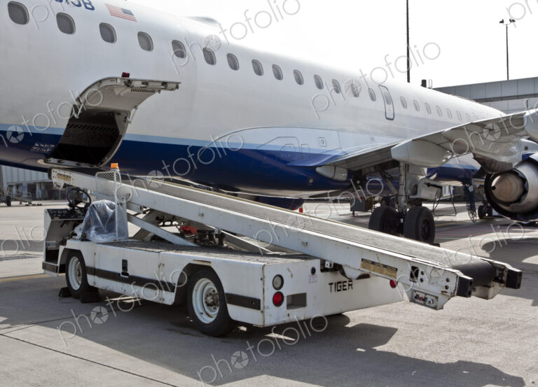 A passenger aircraft on a jetway with a baggage truck vehicle.