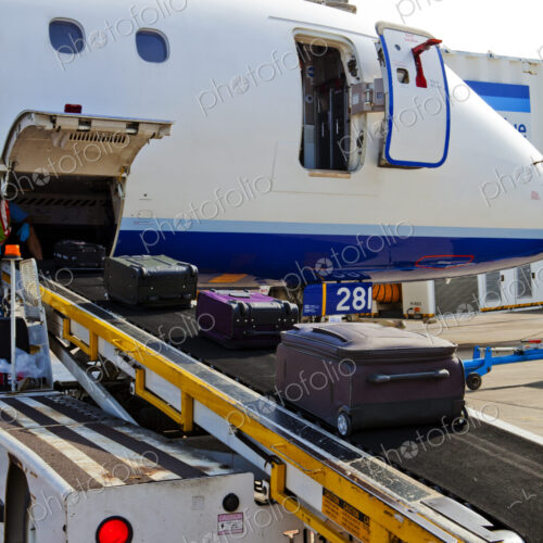 A passenger aircraft on the ground, baggage on a moving belt being loaded