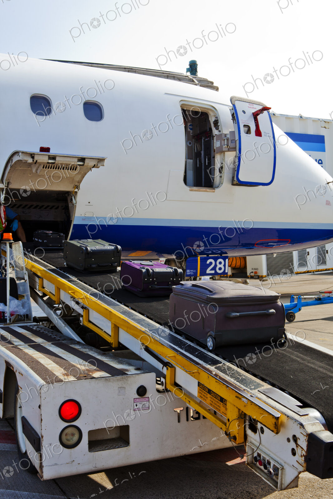 A passenger aircraft on the ground, baggage on a moving belt being loaded