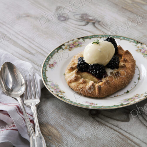 A pastry desert with fruit and icecream on a china plate on a tabletop.