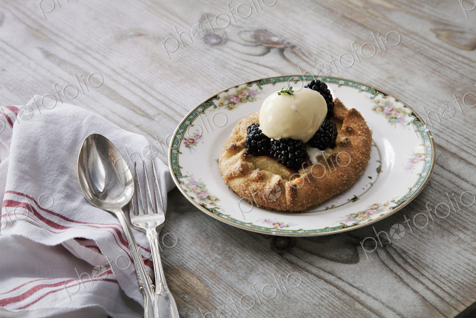 A pastry desert with fruit and icecream on a china plate on a tabletop.
