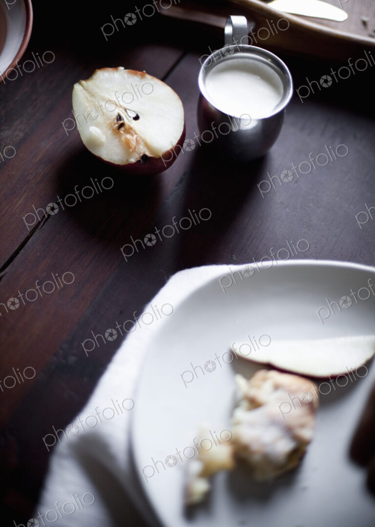 A pear fruit cut open, and sliced. Served on a white china plate. A jug of cream. A…