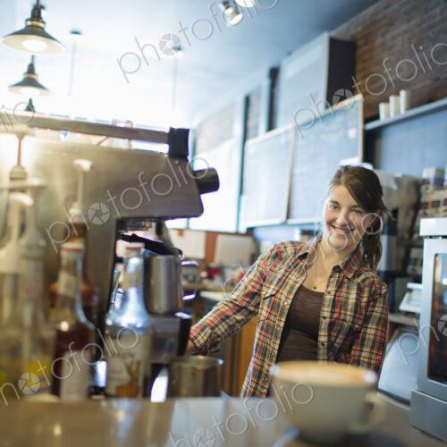 A person, barista, behind the counter at a coffee shop. A large coffee machine for…