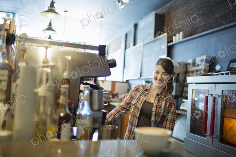 A person, barista, behind the counter at a coffee shop. A large coffee machine for…