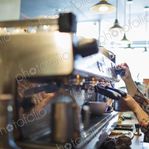 A person, barista making coffee, and frothing milk using a steam pipe, for a…