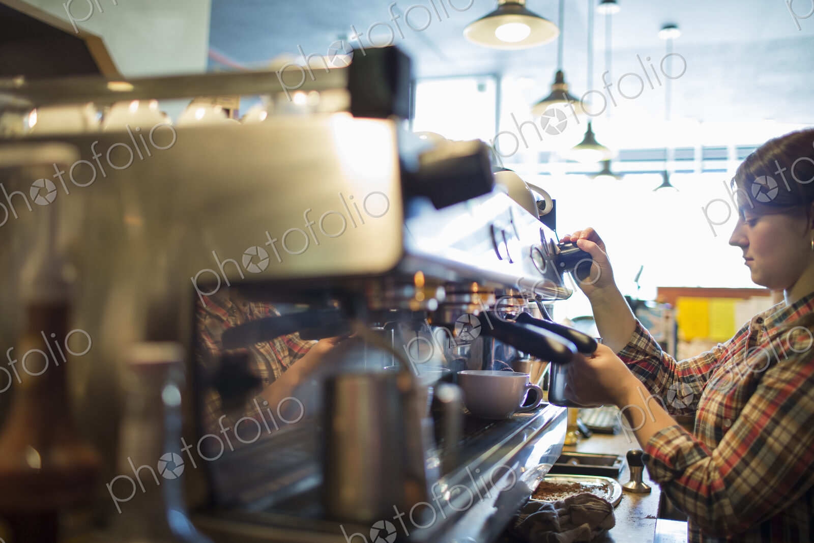 A person, barista making coffee, and frothing milk using a steam pipe, for a…