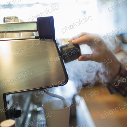 A person, barista making coffee, and frothing milk using a steam pipe. Coffee shop.