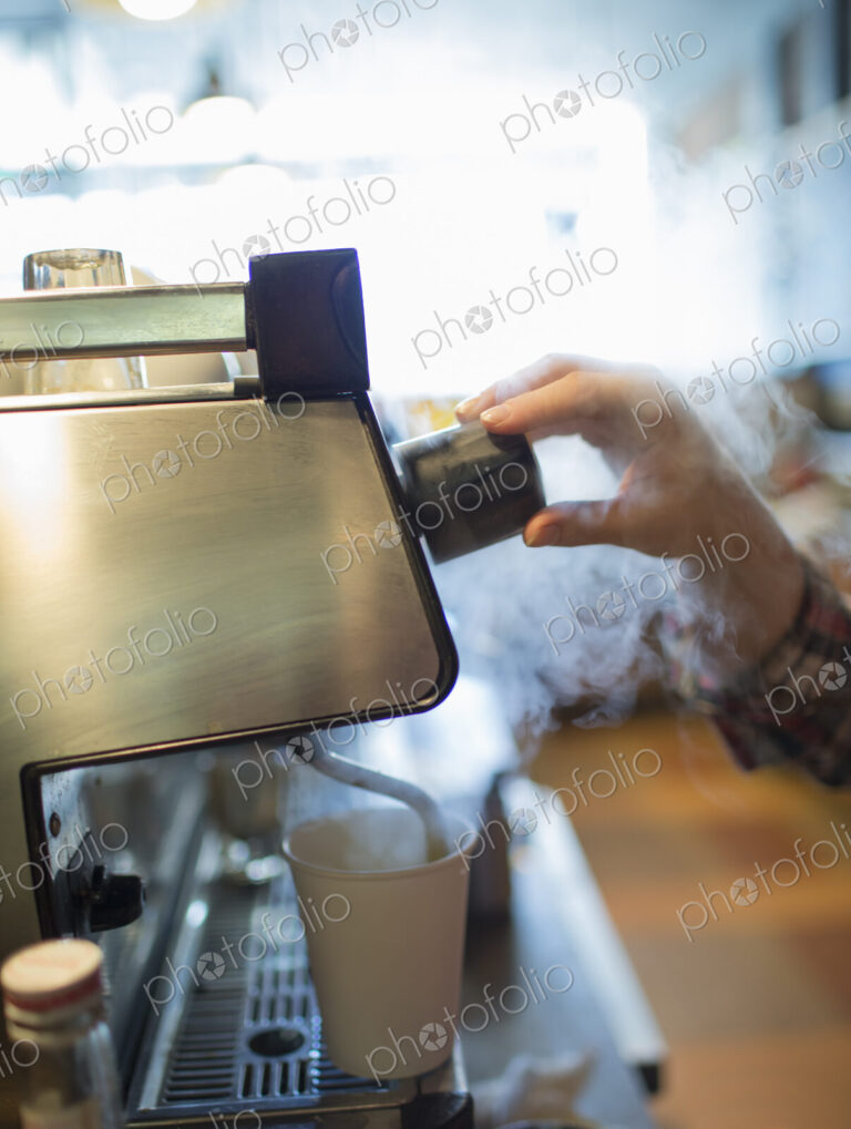 A person, barista making coffee, and frothing milk using a steam pipe. Coffee shop.