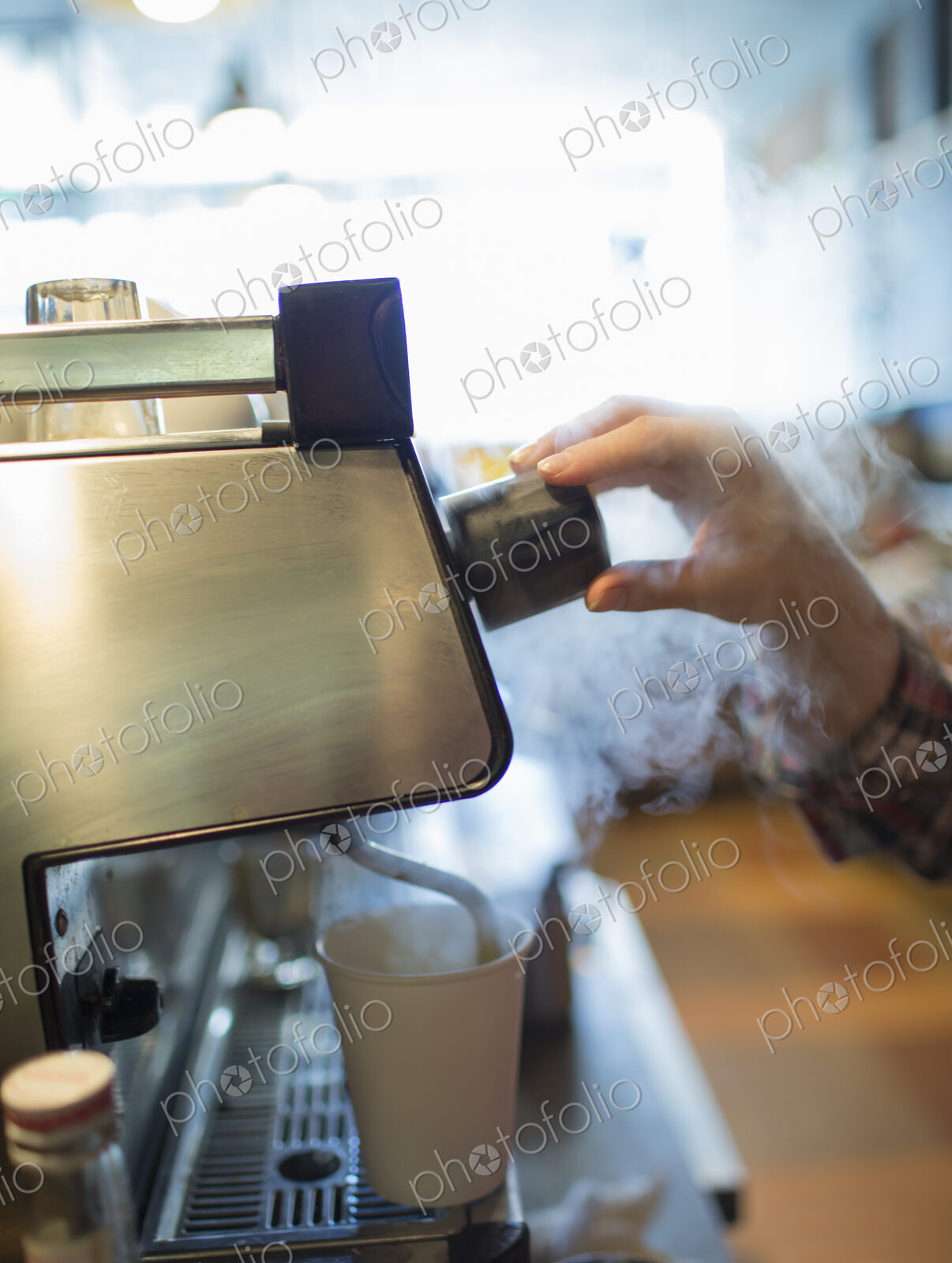 A person, barista making coffee, and frothing milk using a steam pipe. Coffee shop.