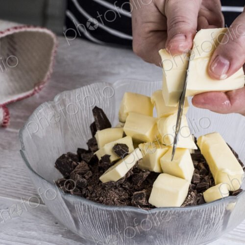 A person cutting chunks of butter into a bowl with pieces of chocolate. A person cutting chunks of butter into a bowl with pieces of chocolate.
