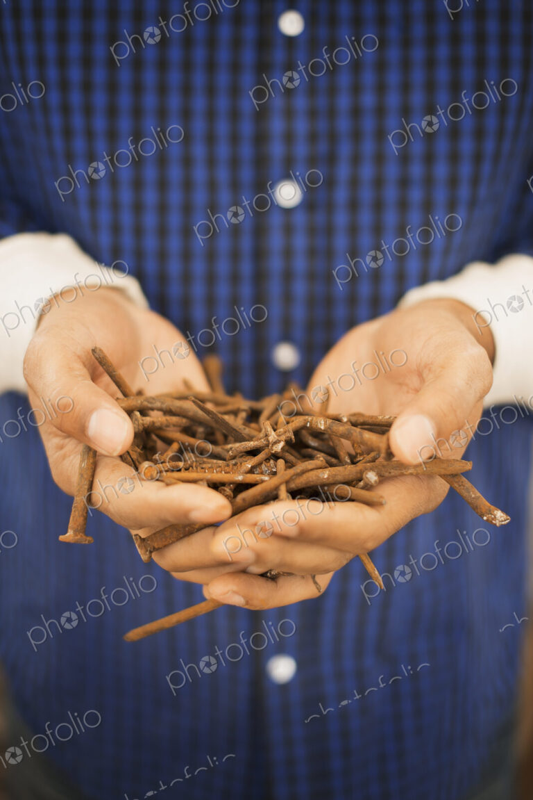 A person holding a heap of rusting metal nails taken from reclaimed timber.