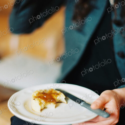 A person holding a plate, holding a half eaten scone with jam.