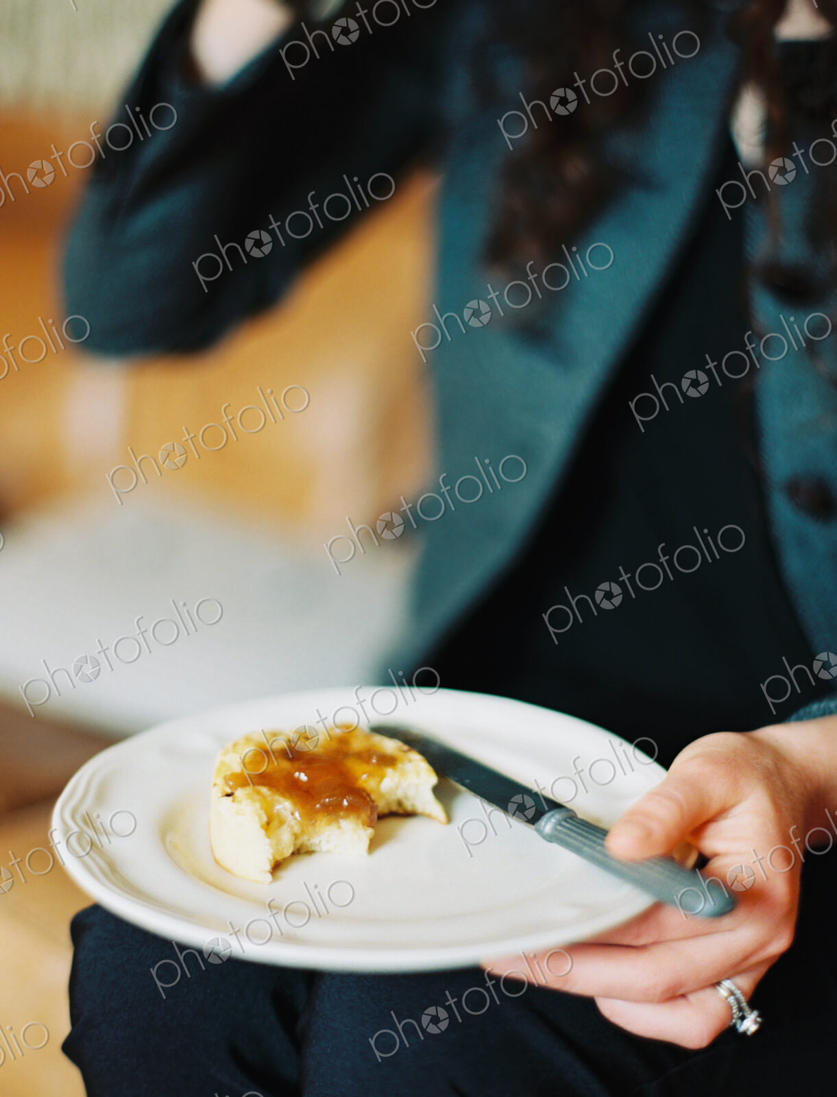 A person holding a plate, holding a half eaten scone with jam.