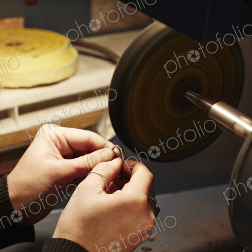 A person holding a small ring and using a grinding machine to shape and polish it.…