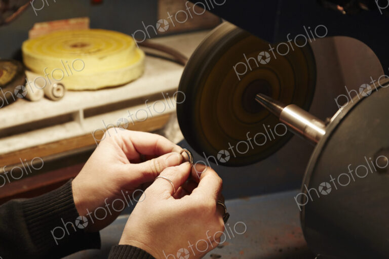 A person holding a small ring and using a grinding machine to shape and polish it.…