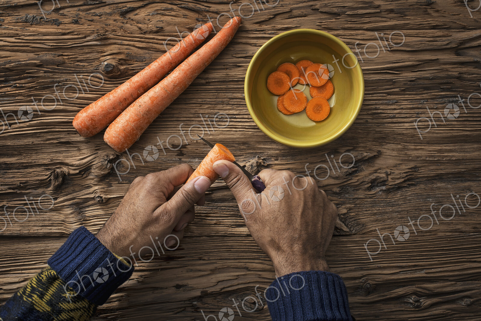 A person holding and slicing fresh carrots into a bowl.