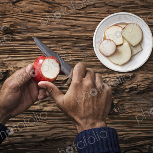 A person holding and slicing sections of a red skinned apple. A person holding and slicing sections of a red skinned apple.