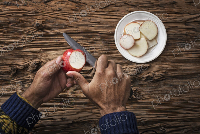 A person holding and slicing sections of a red skinned apple.