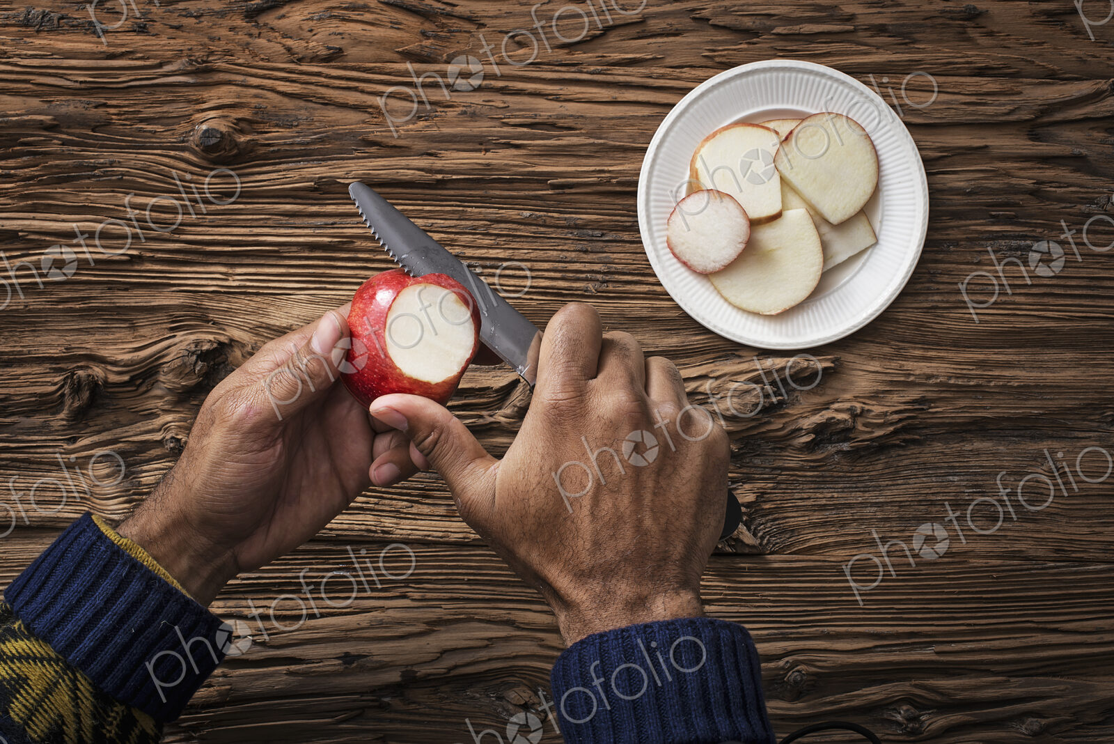 A person holding and slicing sections of a red skinned apple.