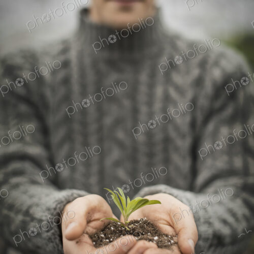 A person in a commercial glasshouse, holding a small plant seedling in his cupped hands.
