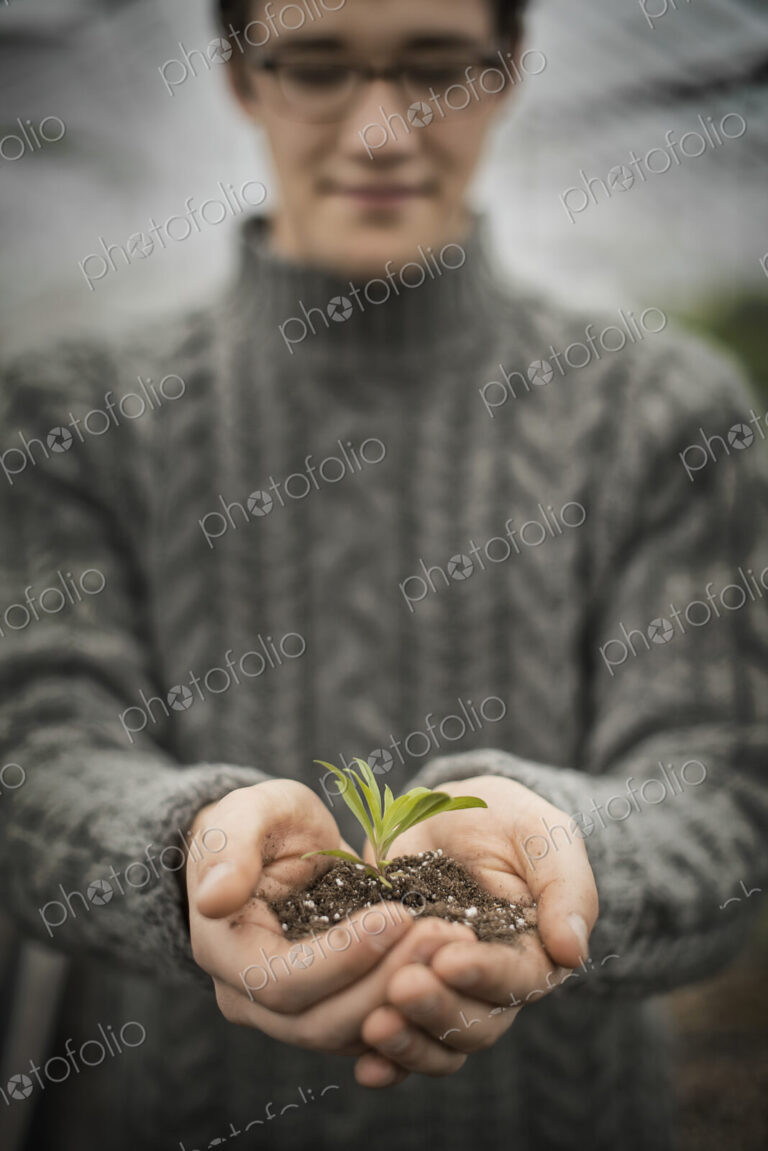 A person in a commercial glasshouse, holding a small plant seedling in his cupped hands.