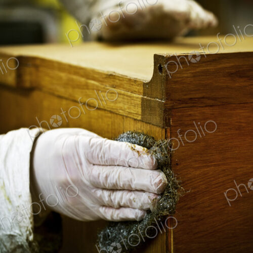 A person in gloves using wire wool to sand down or wax a piece of furniture. A person in gloves using wire wool to sand down or wax a piece of furniture.