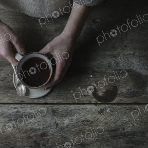 A person lifting a full cup from a saucer.