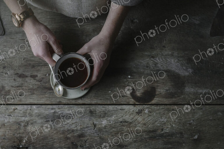 A person lifting a full cup from a saucer.