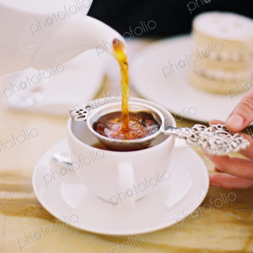 A person pouring a cup of tea, using a strainer. Elegant afternoon tea. A person pouring a cup of tea, using a strainer. Elegant afternoon tea.