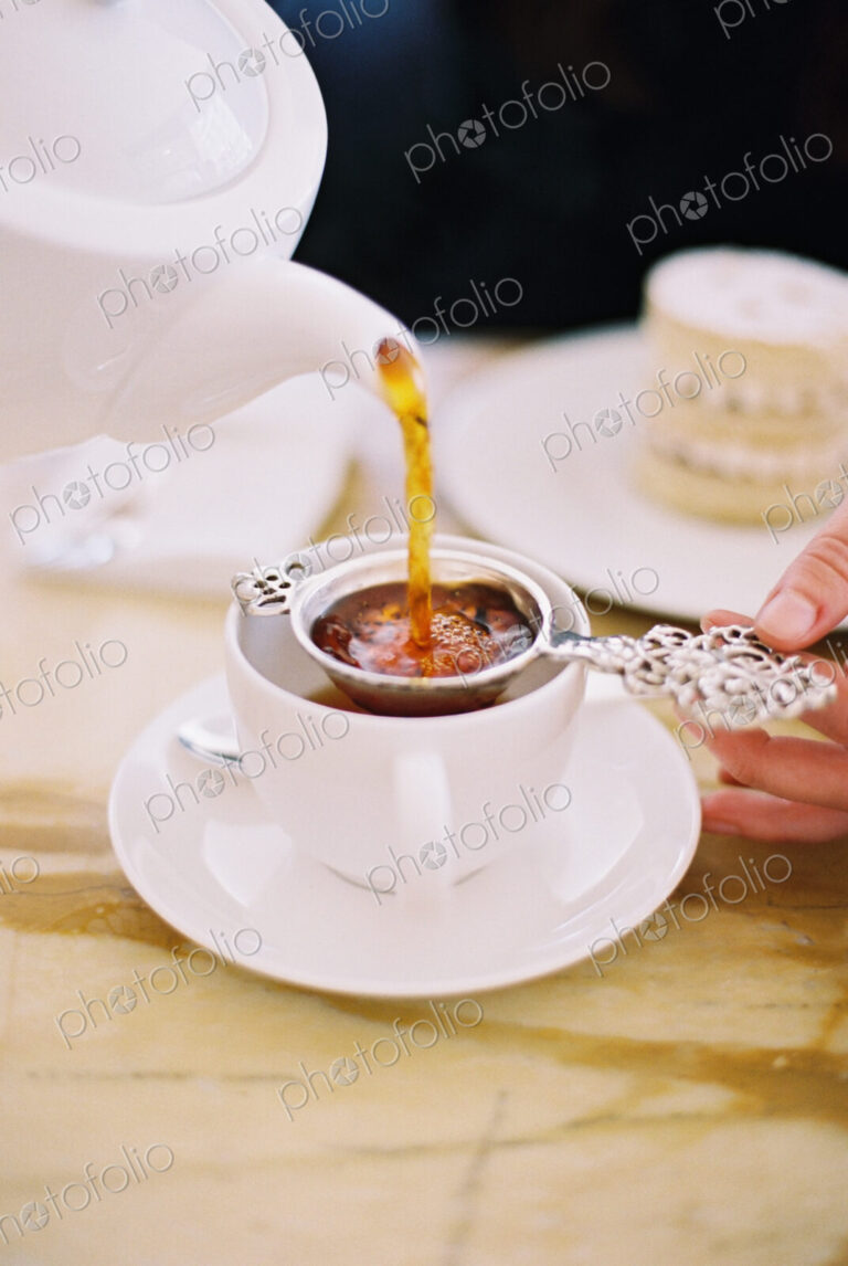A person pouring a cup of tea, using a strainer. Elegant afternoon tea.