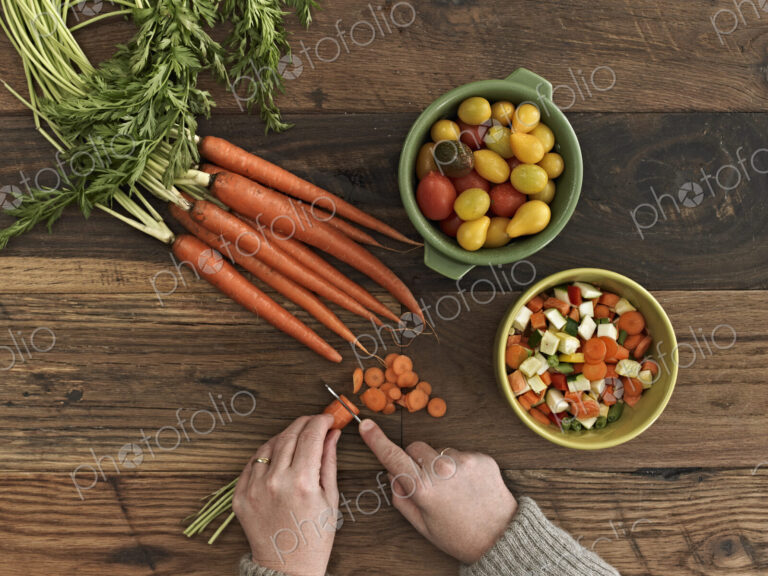 A person preparing fresh vegetables on a wooden table.