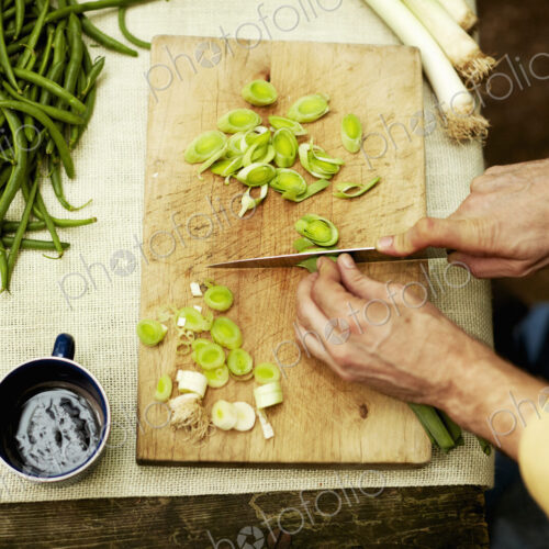 A person preparing vegetables, slicing spring onions on a chopping board. A person preparing vegetables, slicing spring onions on a chopping board.