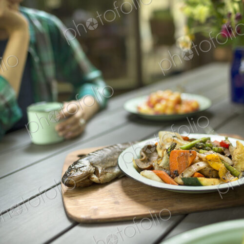 A person seated at a table outdoors. A cooked fresh fish and dish of vegetables. A person seated at a table outdoors. A cooked fresh fish and dish of vegetables.