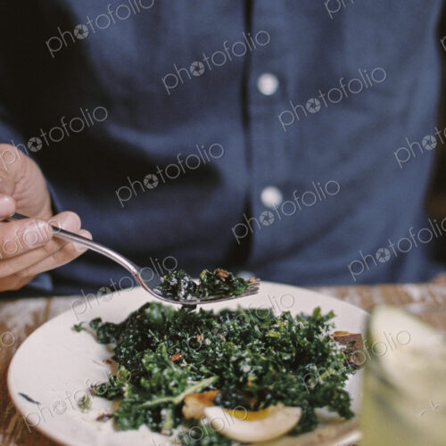 A person seated eating a meal at a table, holding a fork. A person seated eating a meal at a table, holding a fork.