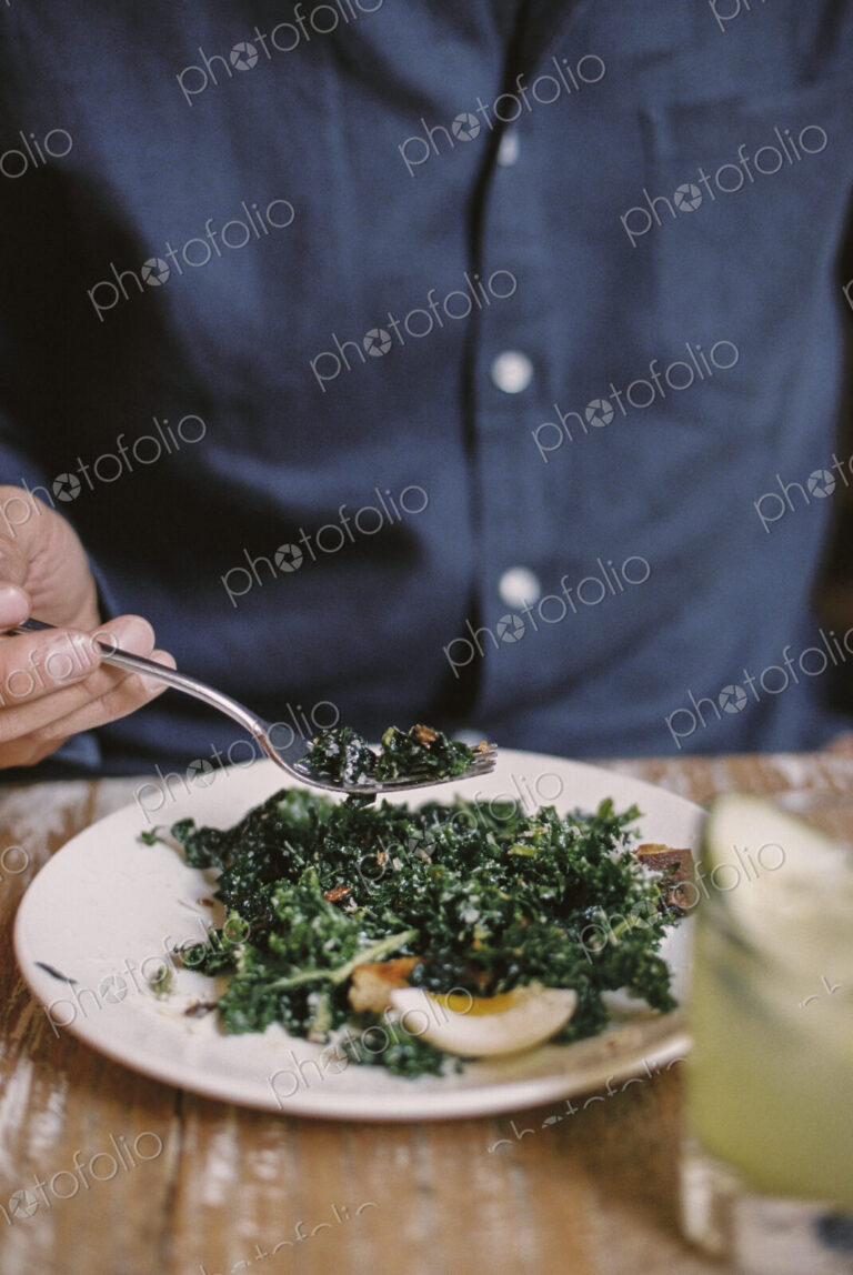 A person seated eating a meal at a table, holding a fork.