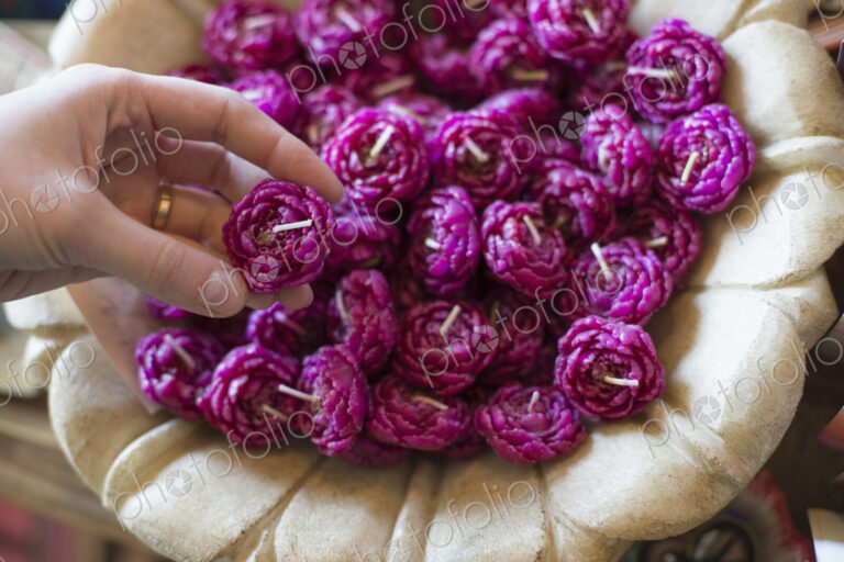 A person selecting a candle from a basket full of purple wax shaped candles.